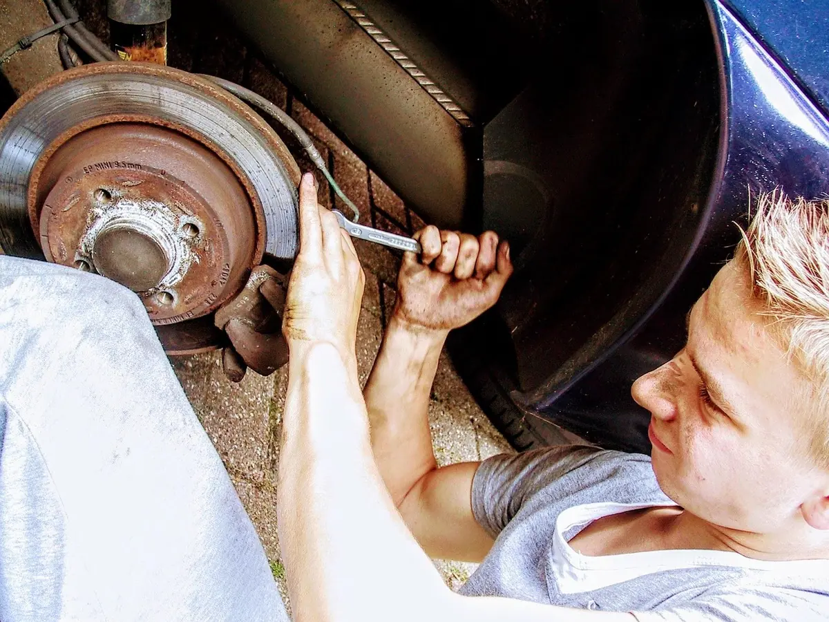 Mechanic reaching behind a rusty brake rotor and wheel hub on a car with the wheel removed