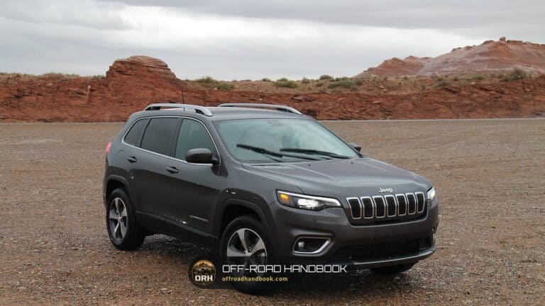 Gray Jeep SUV parked on a dirt lot below red rock hills — Off-Road Handbook