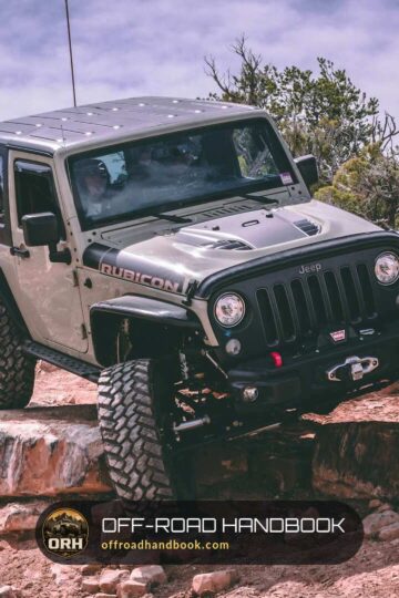 Gray Jeep Wrangler climbing a red rock ledge on a trail