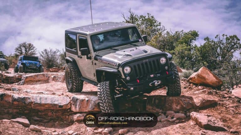 Gray Jeep Wrangler climbing a red rock ledge on a trail