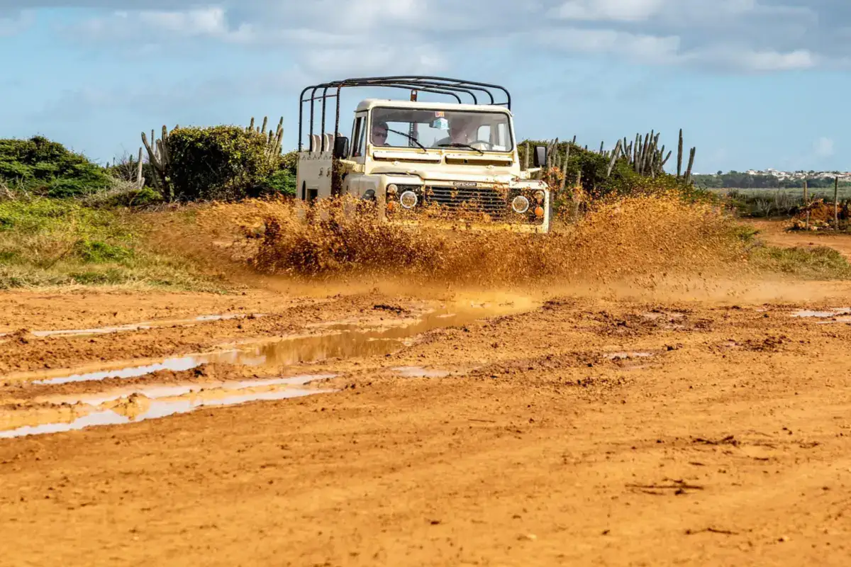 Open-top 4x4 splashing through a muddy dirt road