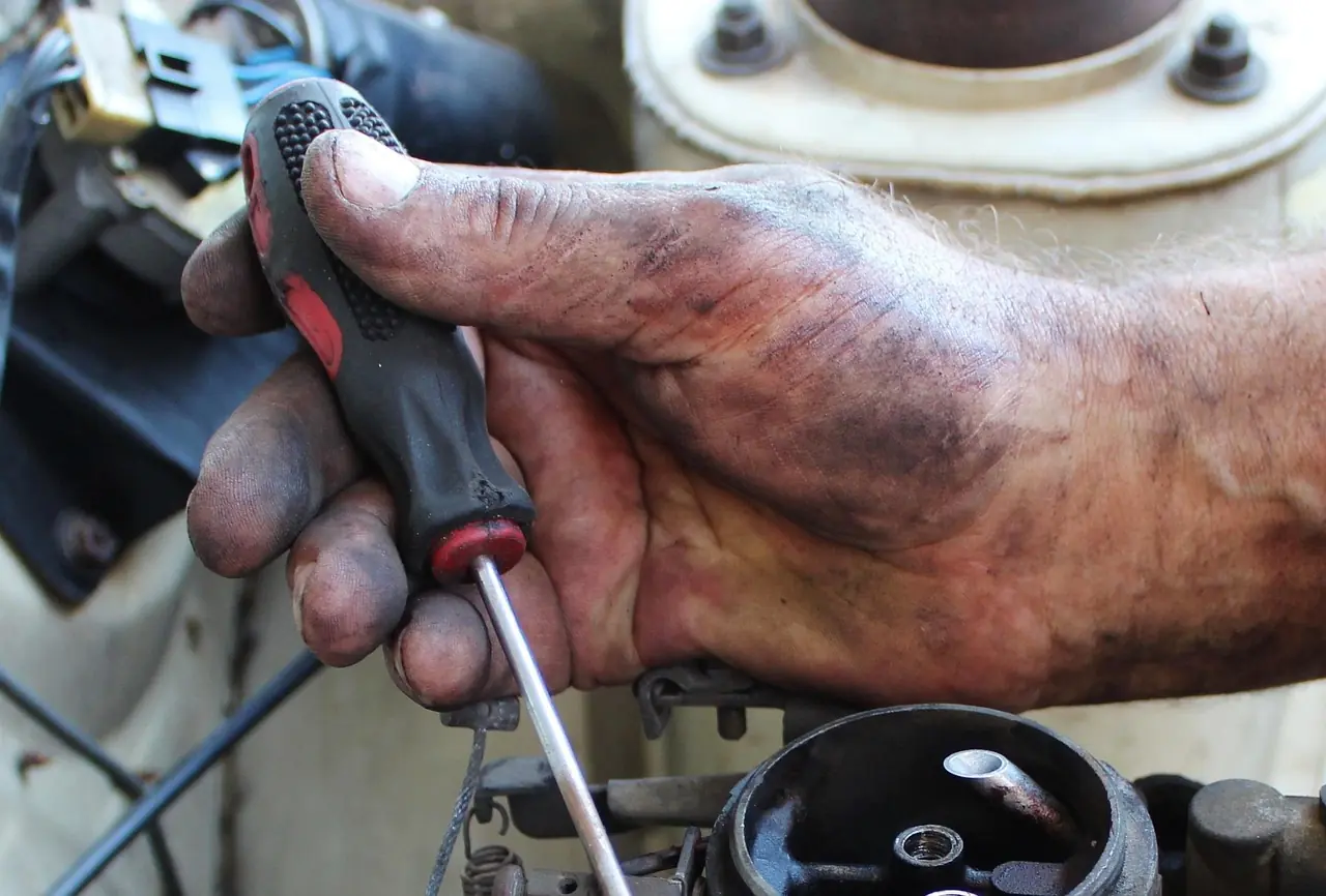 Greasy hand holding a screwdriver while working on an engine
