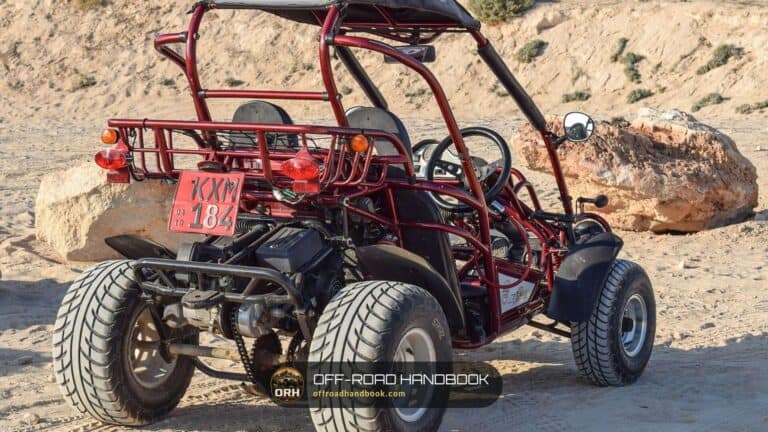 Red open-frame off-road buggy with a roll cage parked on sandy ground