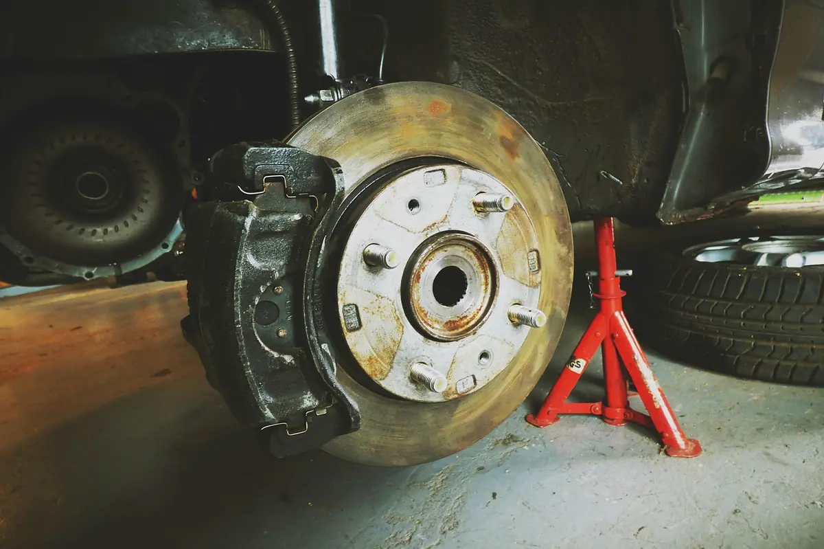 Brake rotor and caliper with a red jack stand supporting the vehicle in a garage