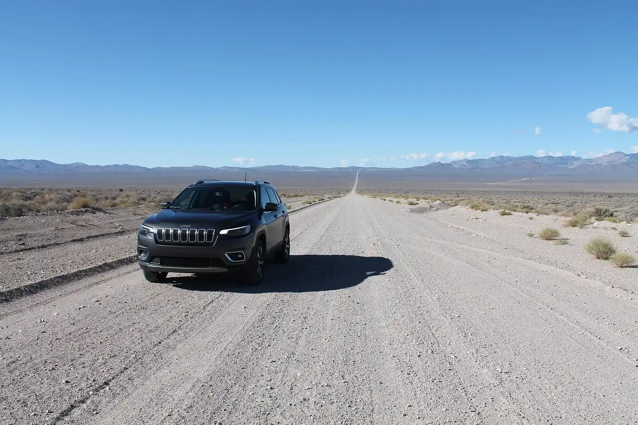 Dark gray Jeep Cherokee SUV parked on a long gravel road crossing a desert valley