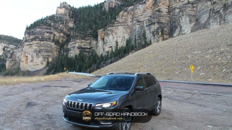 Dark gray Jeep Cherokee SUV parked on gravel below a tall rock cliff