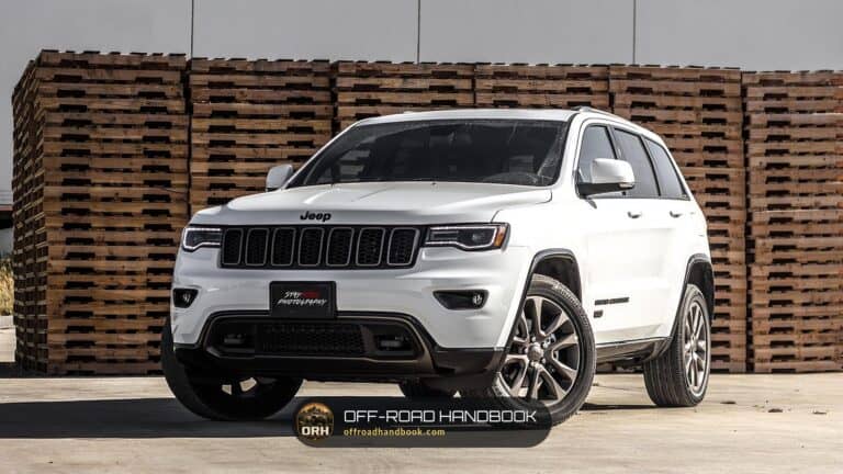 White Jeep Grand Cherokee SUV parked on a concrete lot in front of stacked wooden pallets