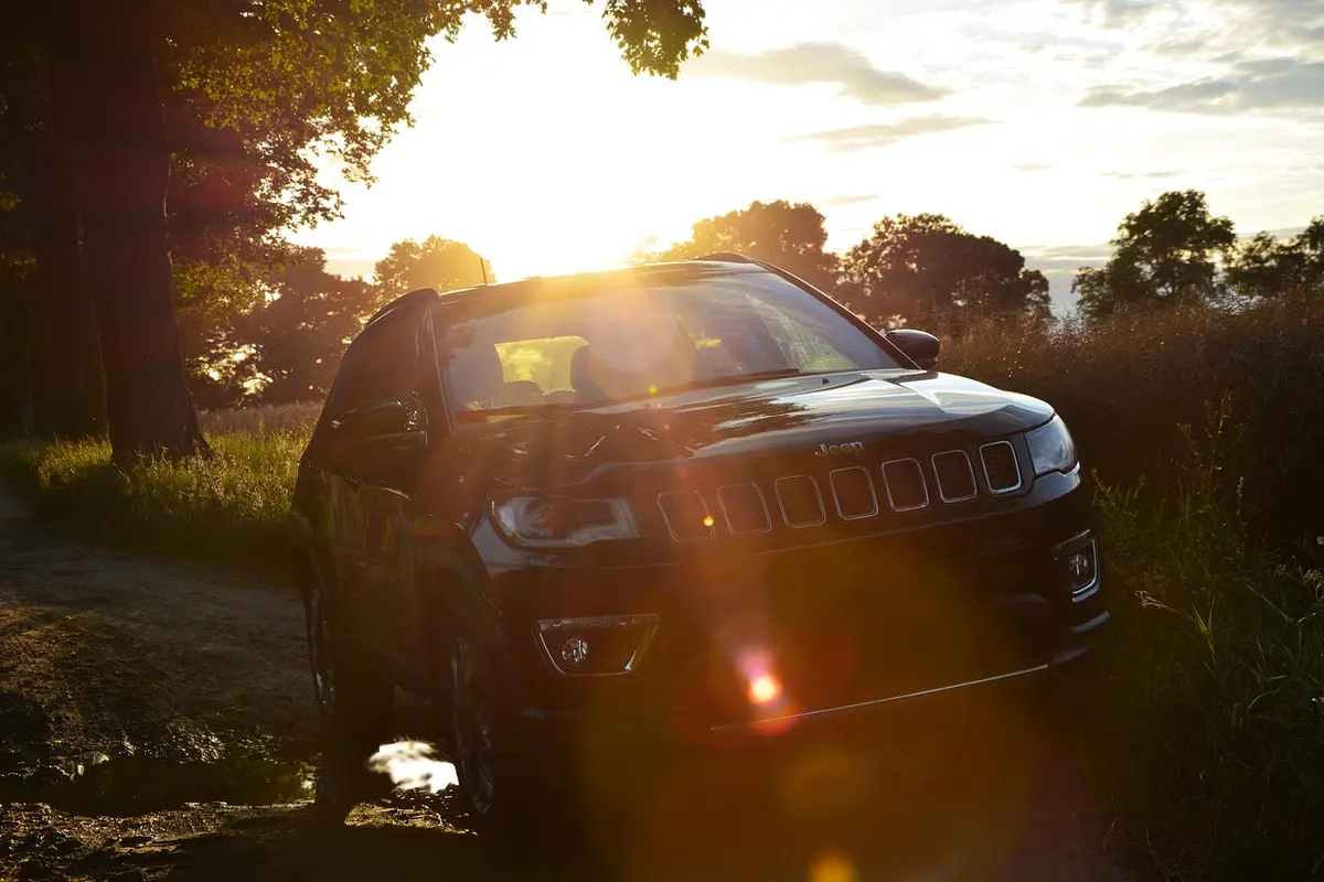 A Jeep Compass SUV parked on a dirt track at sunset