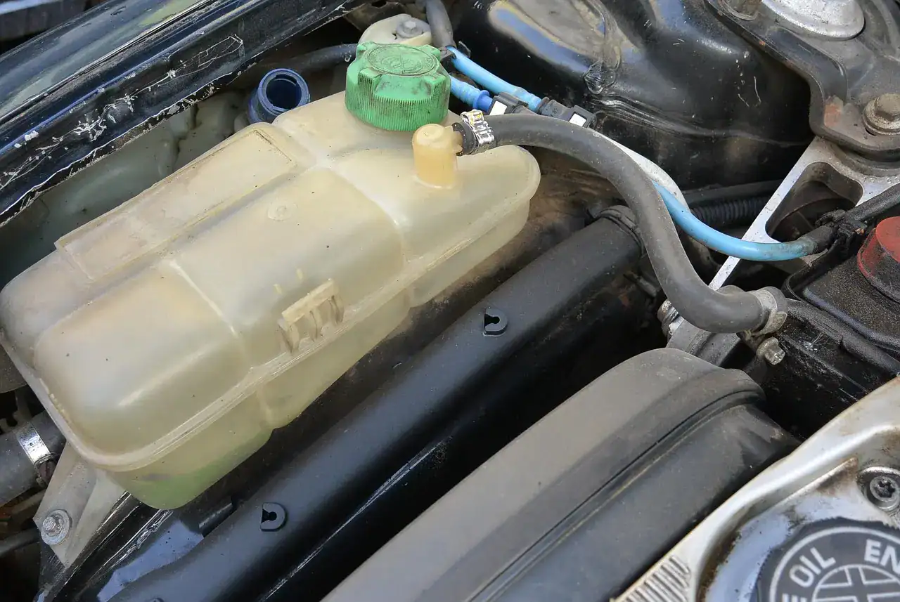 Translucent plastic coolant expansion tank with a green cap and hoses in a car engine bay (not a Wrangler)