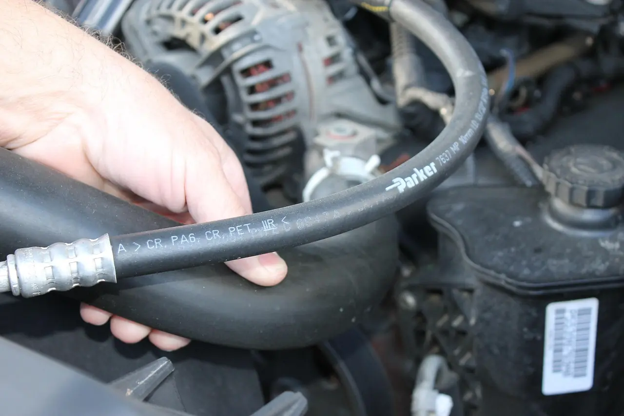 Hand holding a reinforced rubber hose in a car engine bay, similar to the boost and coolant hoses inspected on a turbodiesel
