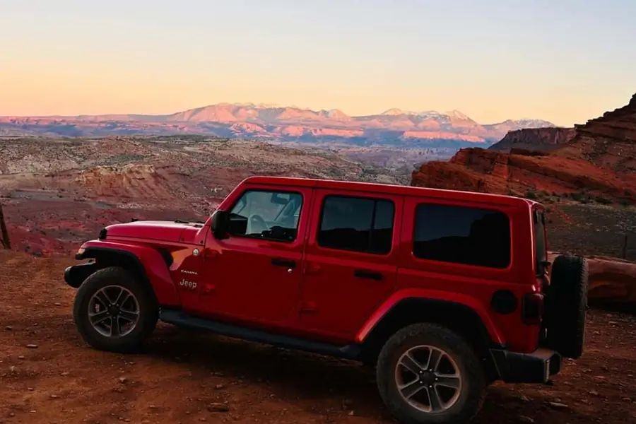 Red Jeep Wrangler Unlimited Sahara on a dirt overlook at sunset