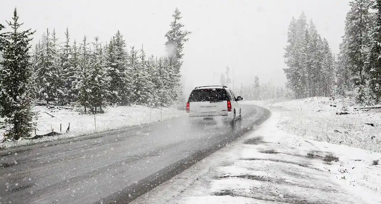 An SUV driving on a snow-covered road through evergreen trees in a snowstorm