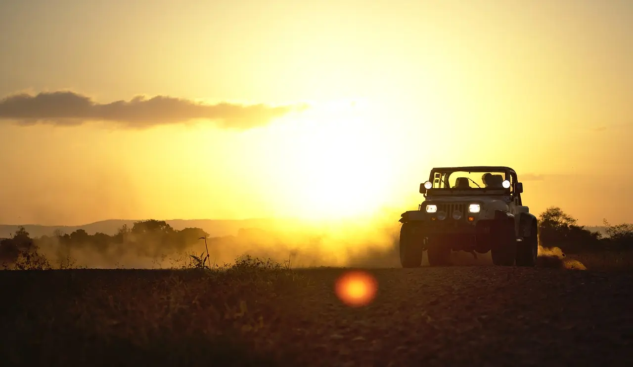 Silhouette of an open Jeep Wrangler on a dusty road at sunset