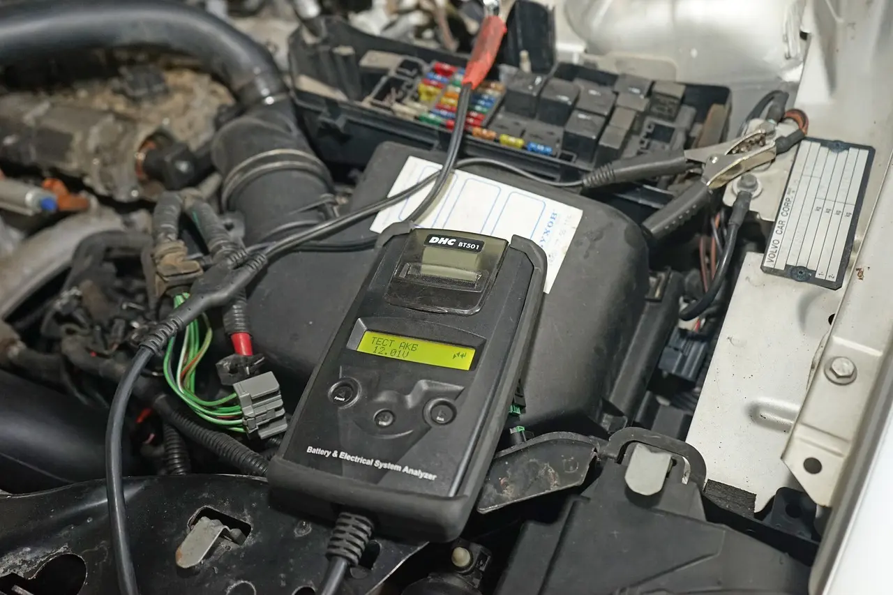 A handheld battery and electrical system analyzer clamped to a car battery in an engine bay