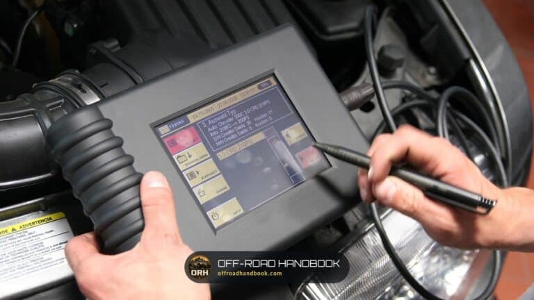A mechanic holding a handheld diagnostic scan tool with a touchscreen and stylus in front of an open engine bay