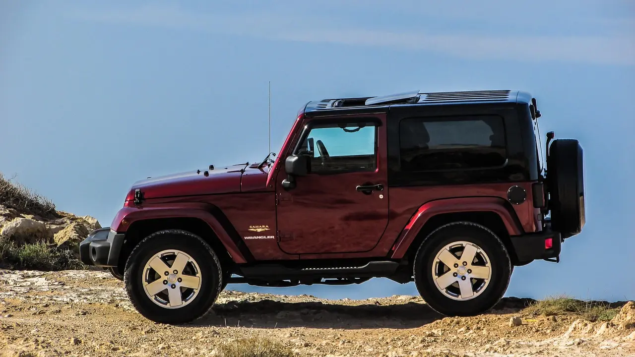 Red two-door Jeep Wrangler parked on a rocky ridge under a clear blue sky