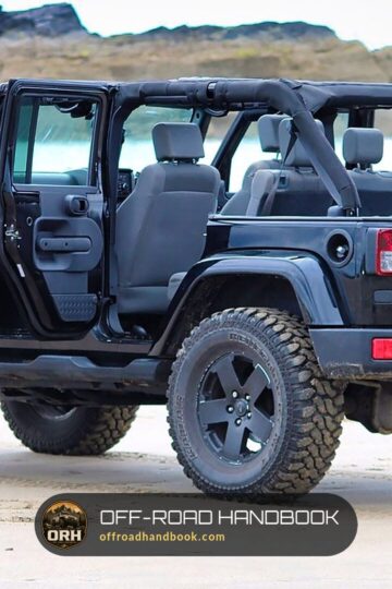 Dark gray four-door Jeep Wrangler Unlimited with doors off and large all-terrain tires parked on a sandy beach