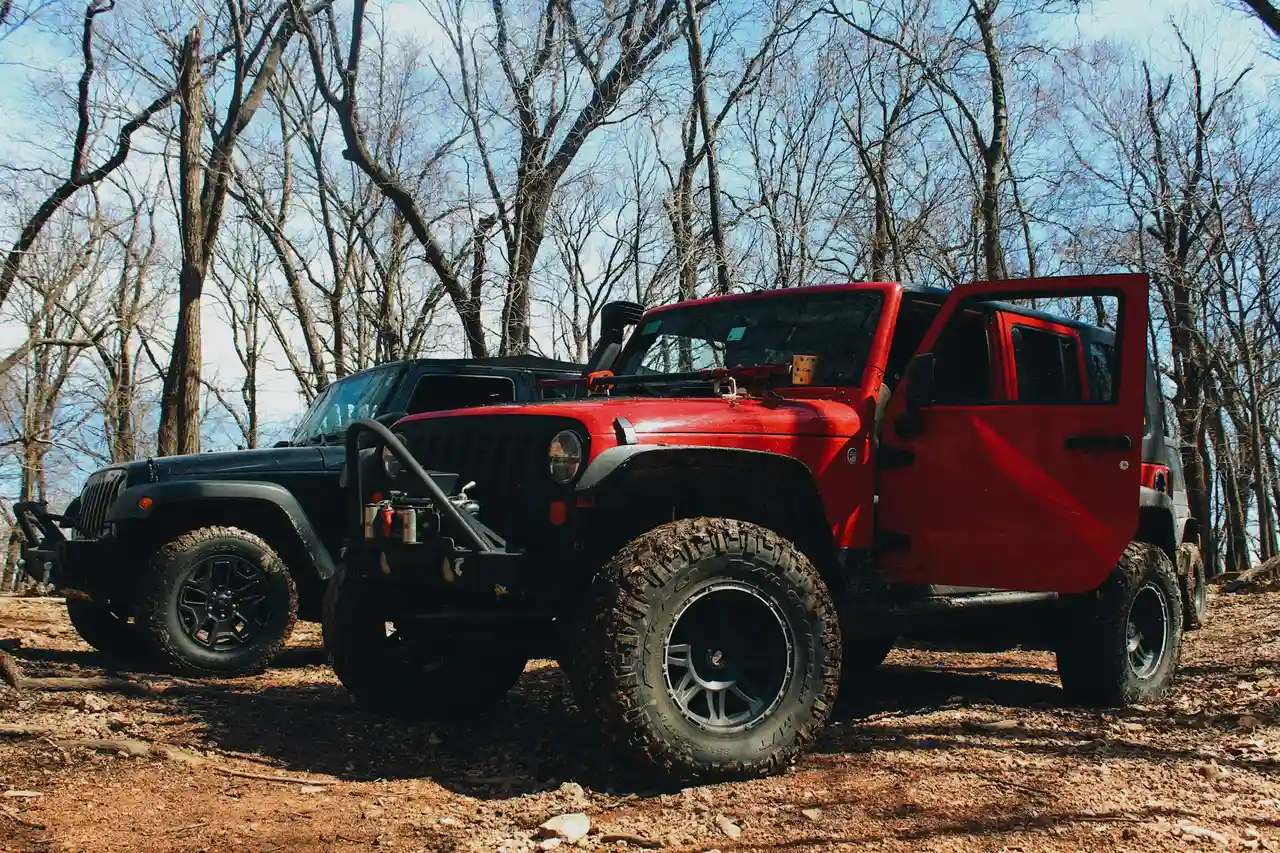 Red Jeep Wrangler with its driver door standing open on a dirt trail