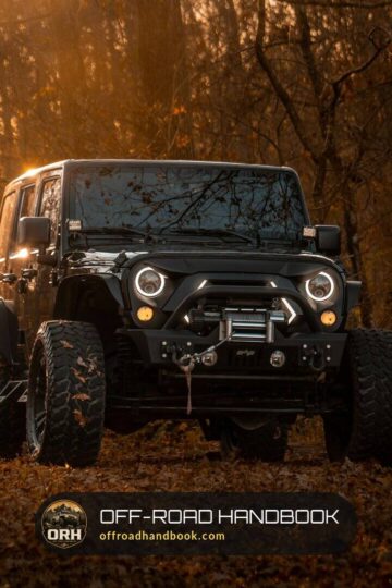 Black Jeep Wrangler with a winch bumper on a forest trail at dusk