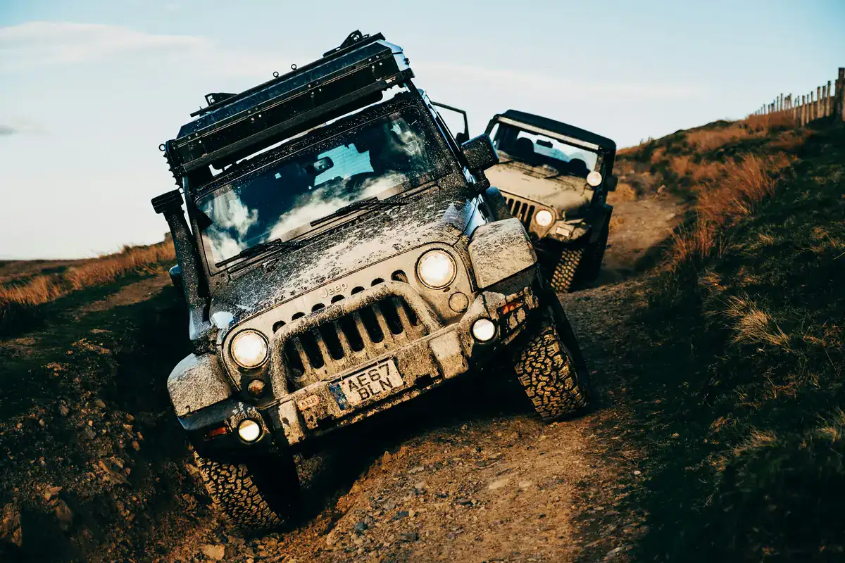 Two muddy Jeep Wranglers climbing a deeply rutted dirt trail