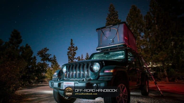 Jeep Wrangler parked at night under a starry sky with a rooftop tent and headlights on