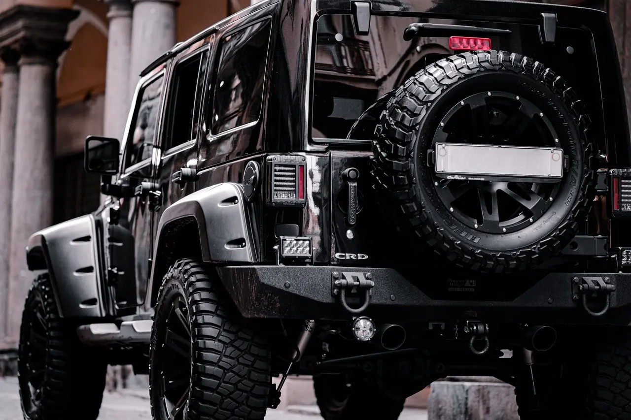 Rear three-quarter view of a black four-door Jeep Wrangler with wide off-road tires and a mounted spare