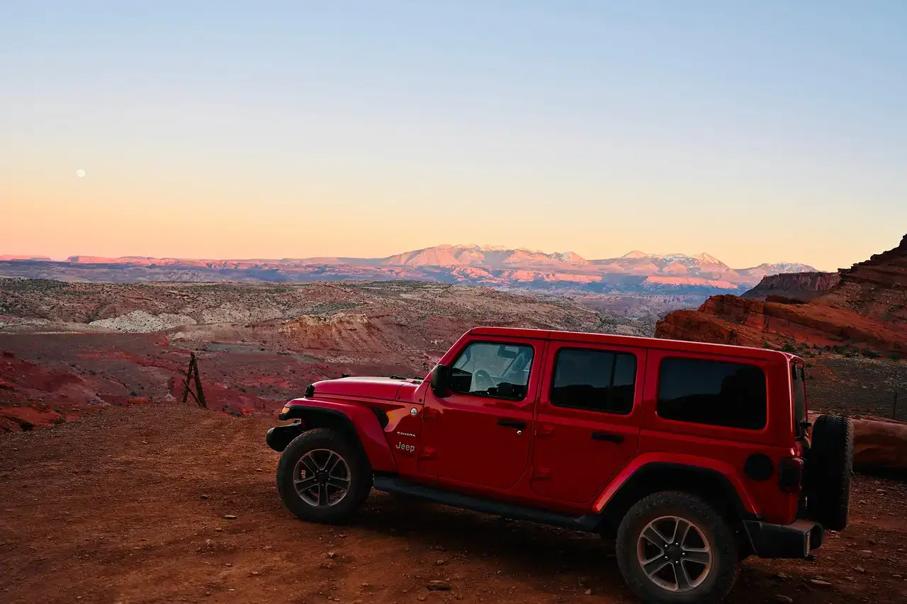 A red four-door Jeep Wrangler parked on a desert plateau at dusk