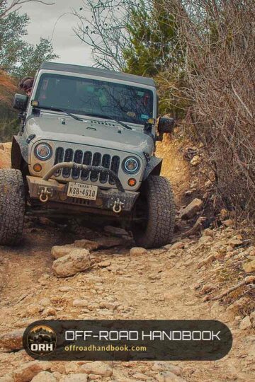 Gray Jeep Wrangler JK crawling down a rocky, brush-lined dirt trail toward the camera