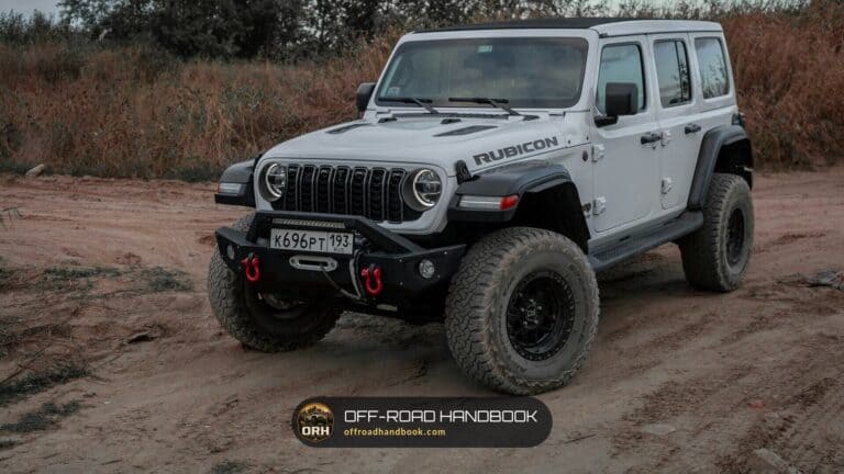 White four-door Jeep Wrangler Rubicon on large all-terrain tires parked on a dirt road