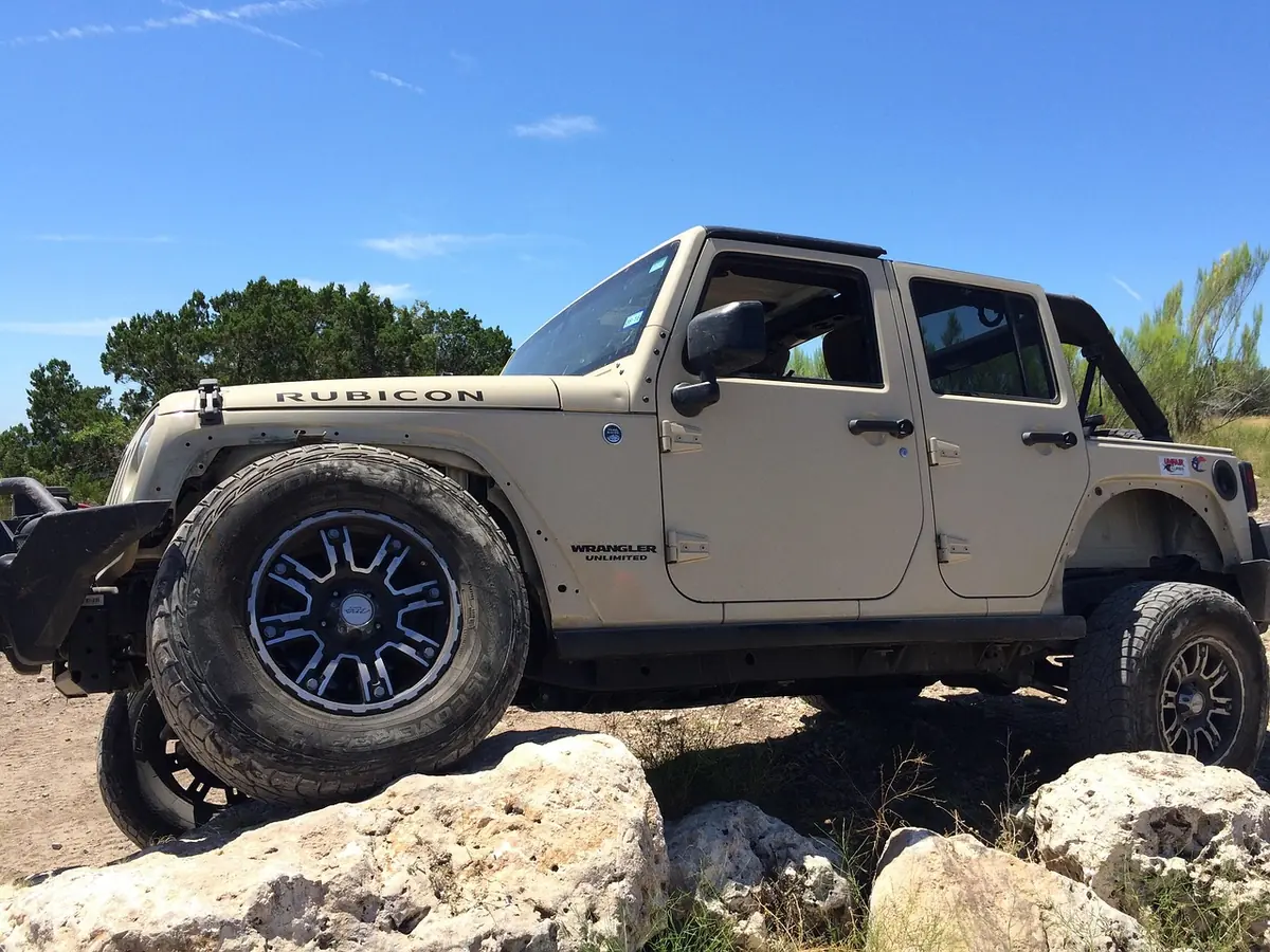 Four-door Jeep Wrangler Rubicon with a front wheel up on large rocks on a trail