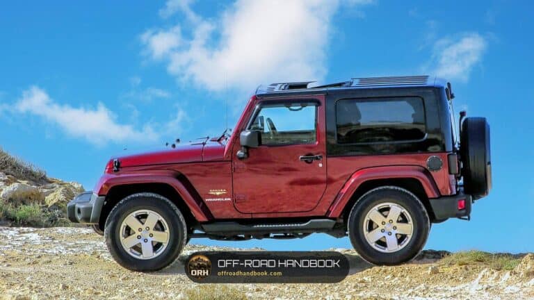 Red two-door Jeep Wrangler Sahara parked on rocky ground under a blue sky