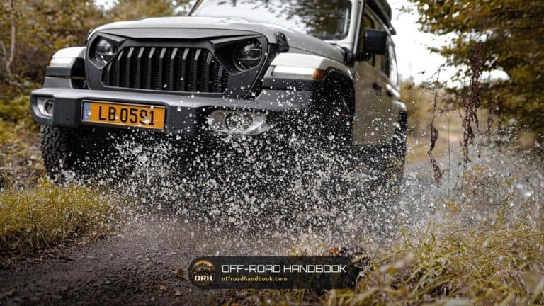 Gray Jeep Wrangler splashing through water on a forest trail — Off-Road Handbook