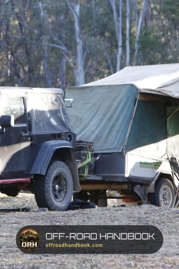 Two-door Jeep Wrangler JK hitched to an off-road camper trailer at a forest campsite