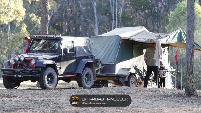 Two-door Jeep Wrangler JK hitched to an off-road camper trailer at a forest campsite