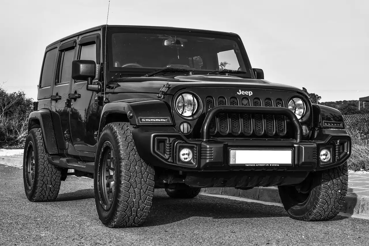 Black and white front three-quarter view of a four-door Jeep Wrangler with large off-road tires