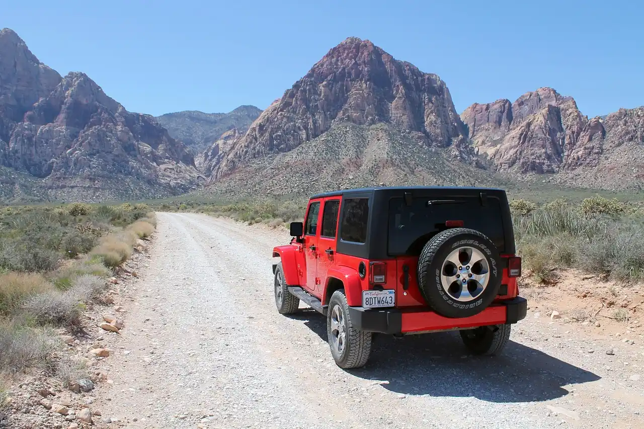 Red four-door Jeep Wrangler on a gravel road leading toward red rock mountains in Nevada