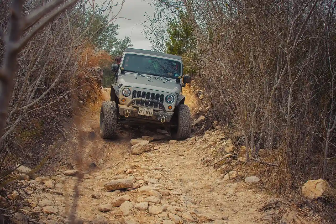 Lifted Jeep Wrangler climbing a rocky dirt trail between dry brush