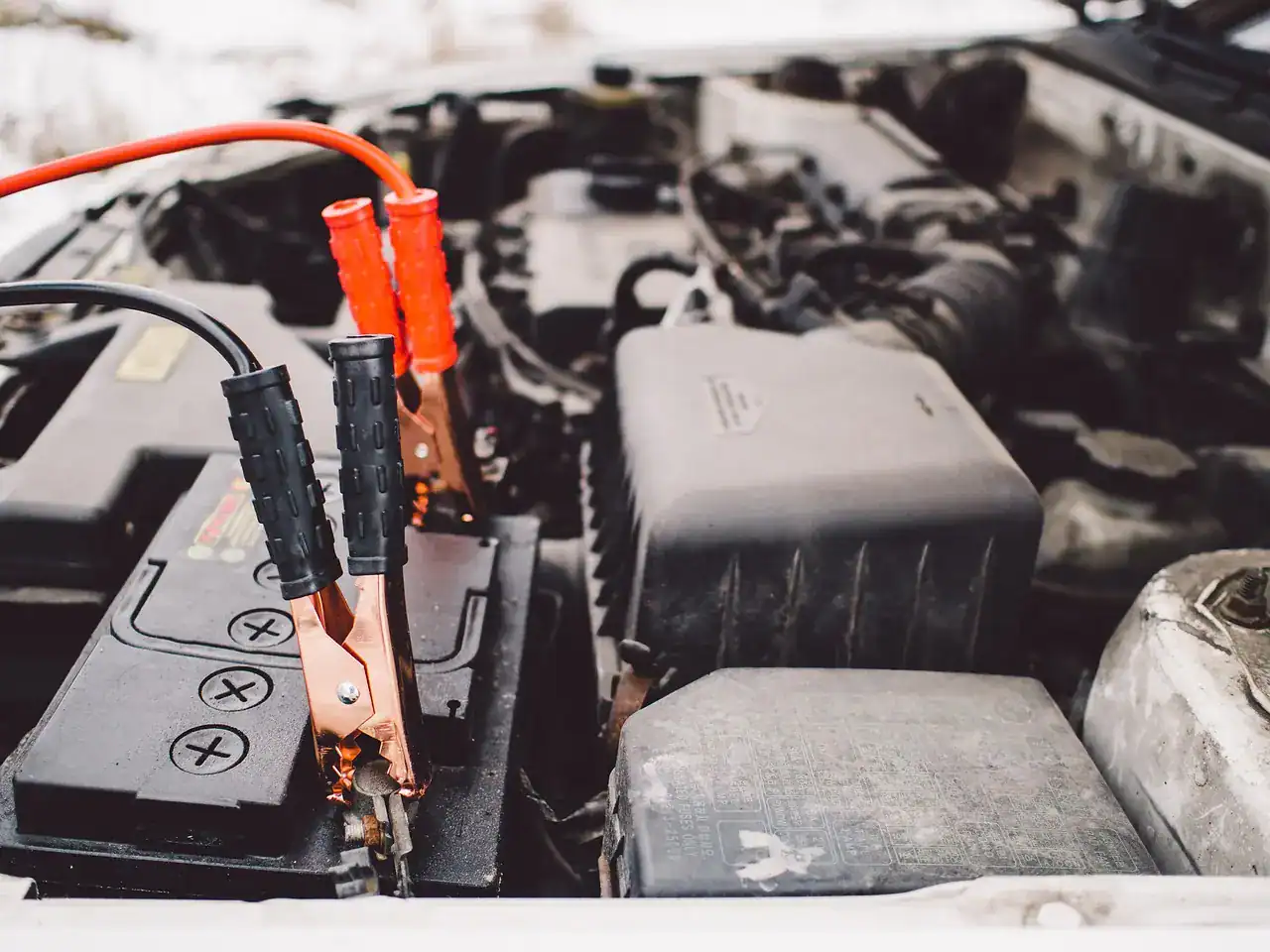 Red and black jumper cable clamps connected to a battery in an engine bay