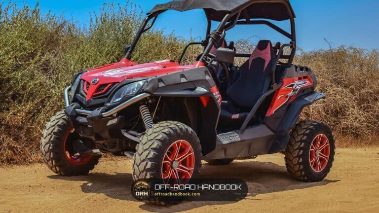 Red side-by-side UTV with knobby tires parked on a dirt trail beside dry brush — Off-Road Handbook