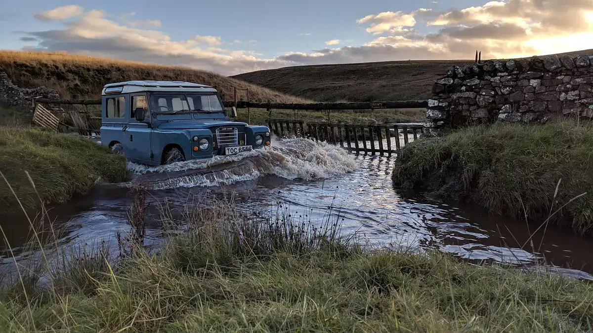 Older blue Land Rover driving through a shallow stream