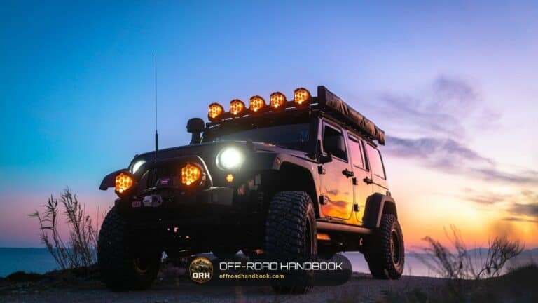 Lifted Jeep with roof-mounted lights and large tires at dusk