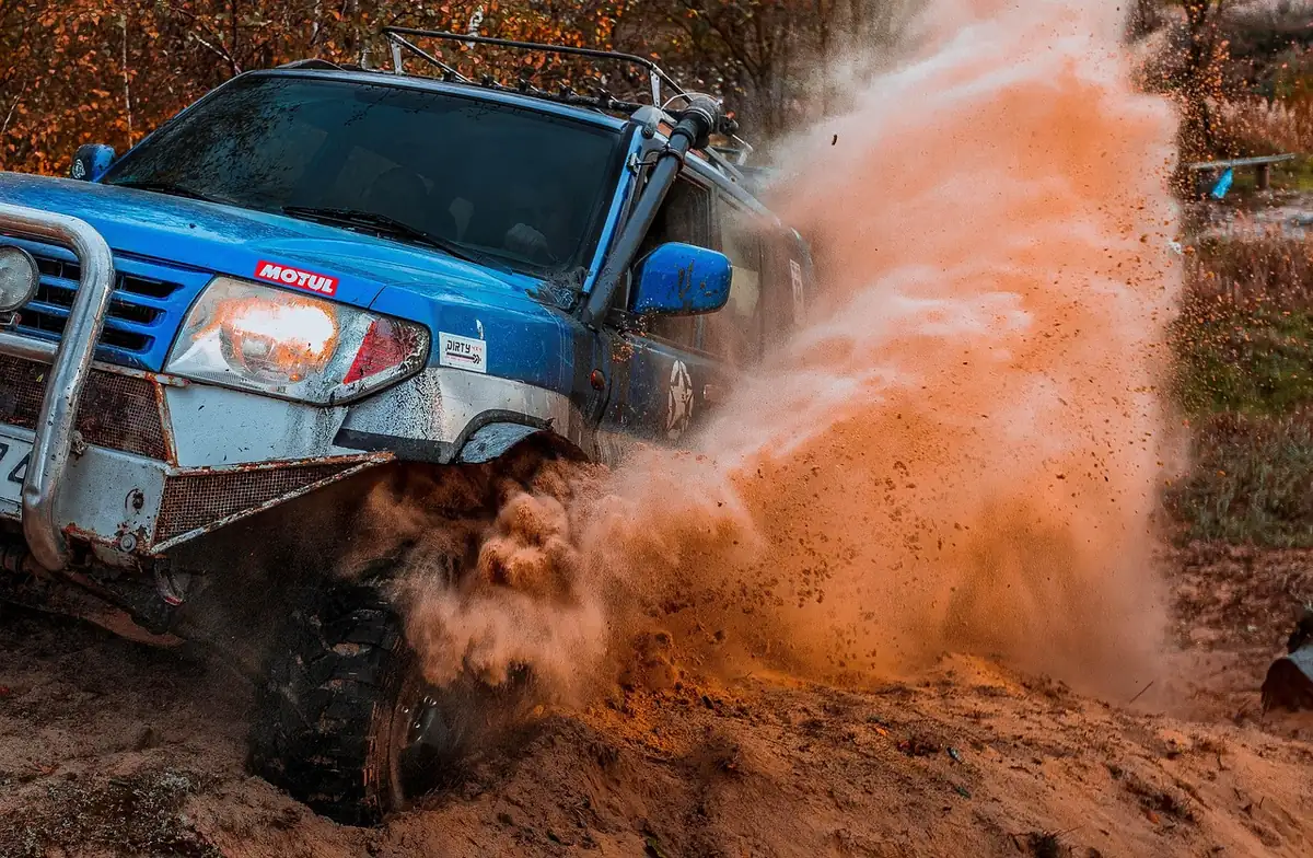 Blue 4x4 with a brush guard throwing orange dust from a spinning front wheel on a loose trail