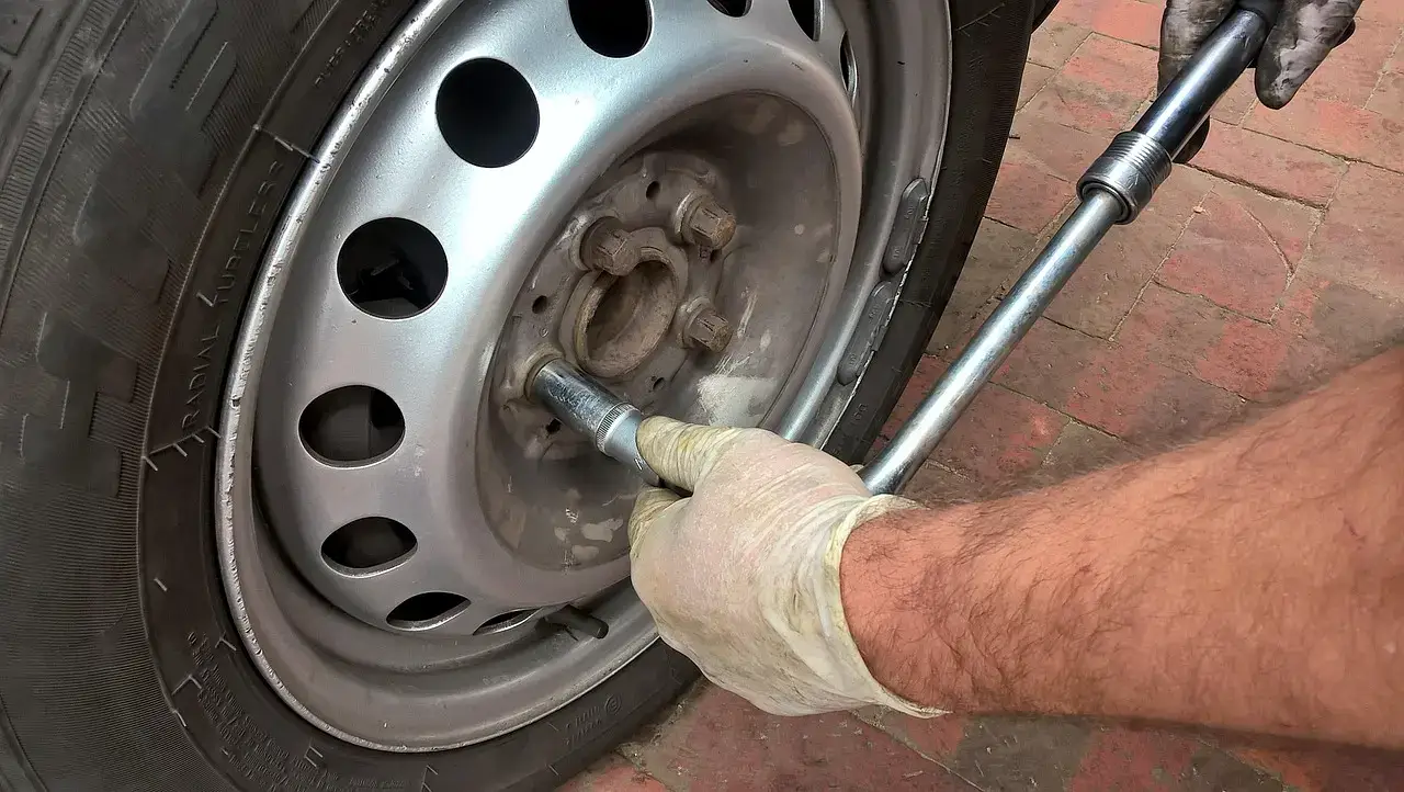 Gloved hand using a long wrench on a lug nut of a steel wheel