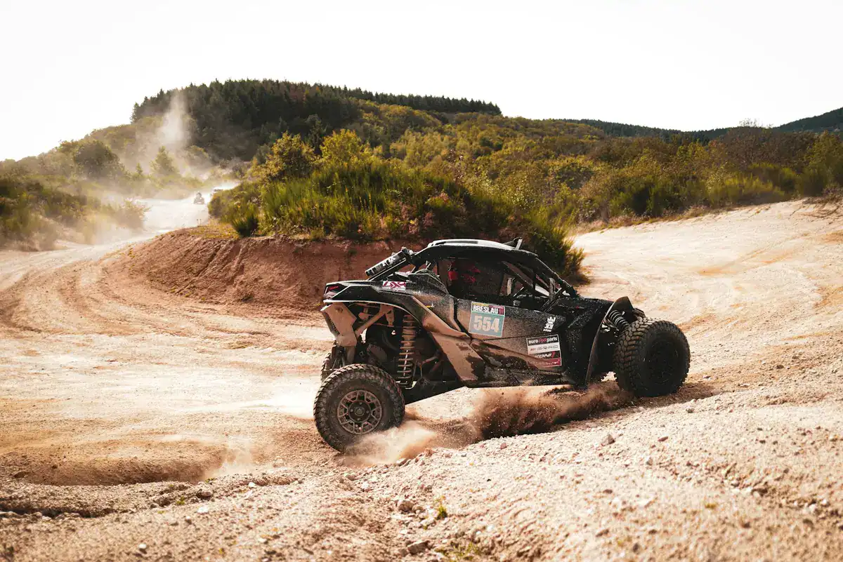 Black Can-Am Maverick X3 race car sliding through a loose, dusty gravel turn