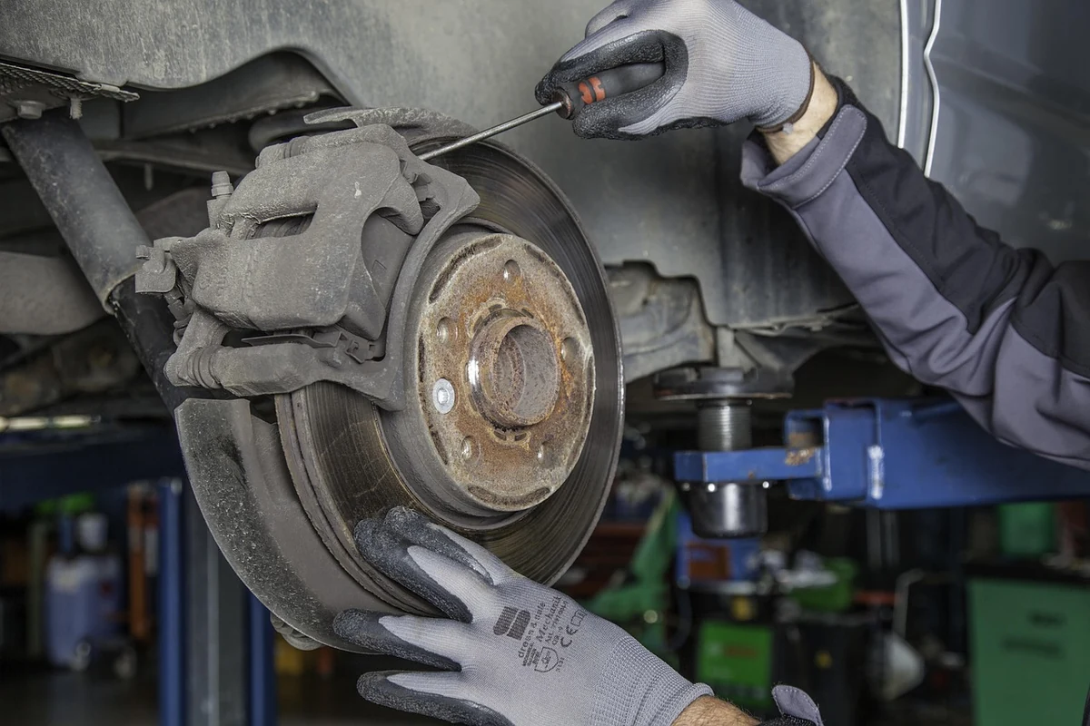 Mechanic's gloved hand with a screwdriver working at a brake caliper and rotor on a car raised on a lift