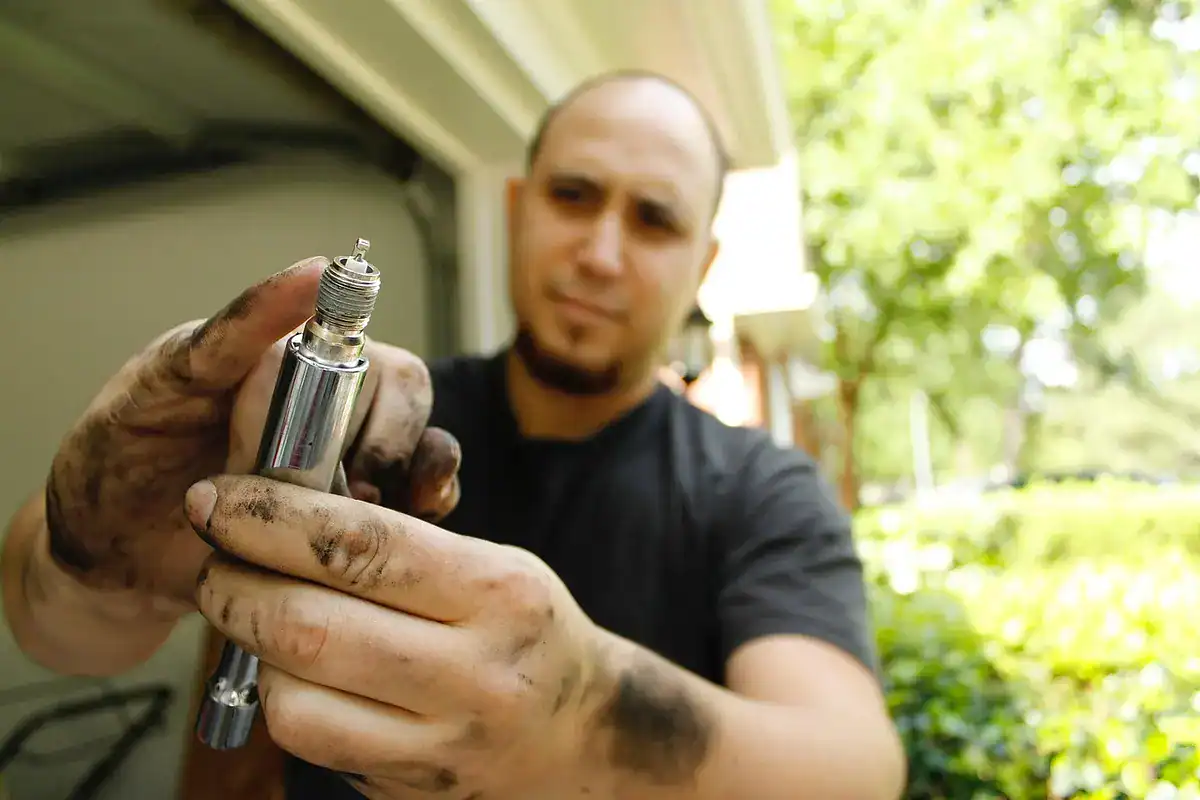 Mechanic with dirty hands holding a spark plug up to inspect it