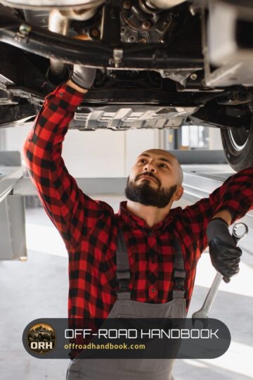 Mechanic in a plaid shirt working on the underside of an SUV raised on a service lift