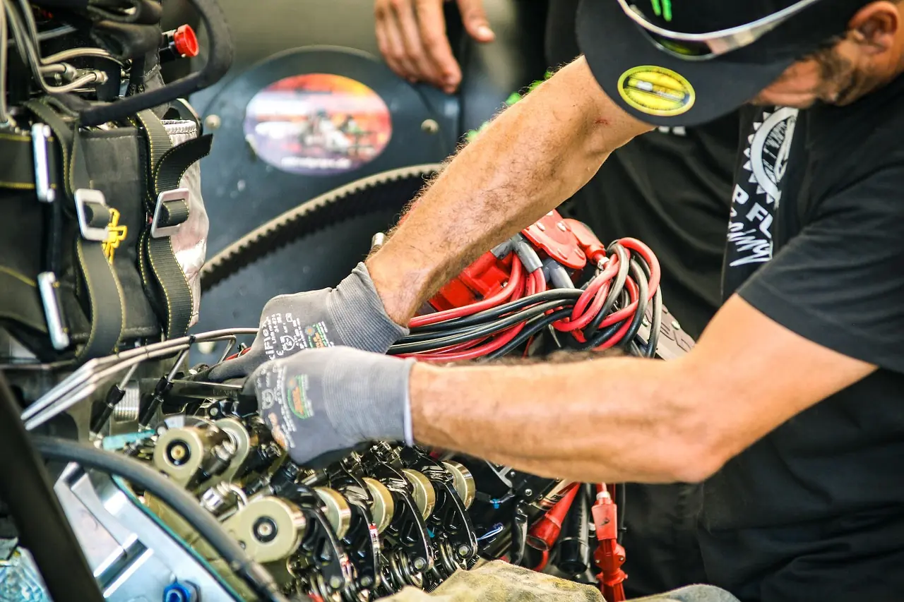 Mechanic in work gloves working on an off-road engine with a drive belt and wiring visible