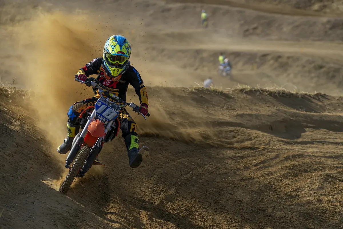 Motocross rider in neon gear leaning a blue bike through a dusty dirt corner
