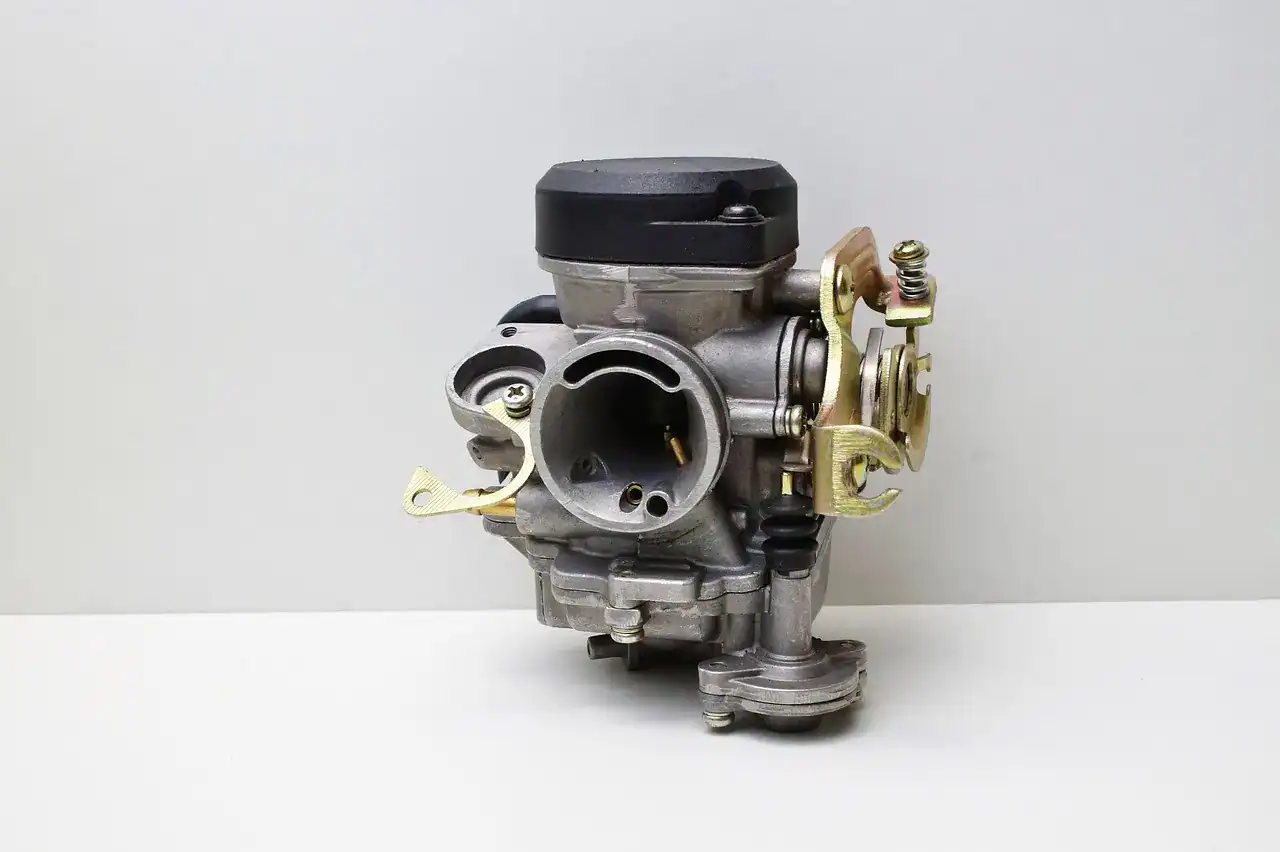 Small single-cylinder carburetor with throttle linkage and float bowl on a plain background